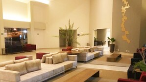 Amplia sala de estar con un sofá seccional grande, una mesa de centro de madera y sillones rojos. Se ven plantas en macetas y una zona de comedor al fondo.