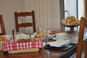 Mesa de desayuno dispuesta con pan, pasteles, un vaso de zumo de naranja y una taza de café.