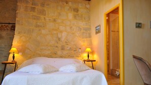 Una camera da letto con parete in pietra, un letto con biancheria bianca, due lampade da comodino e una sedia.