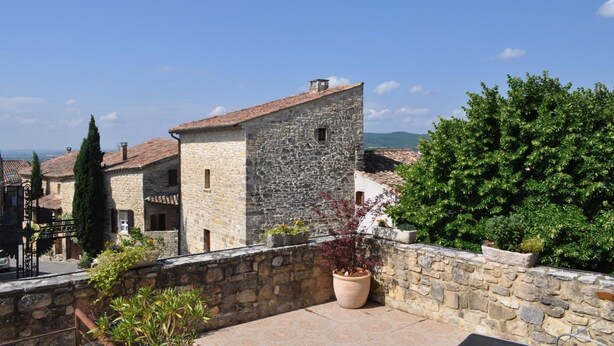 Un edificio in pietra con tetto in tegole, circondato da vegetazione e altri edifici in pietra.