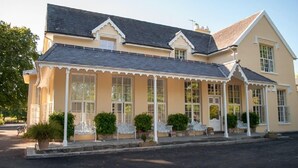 A two-story building with a cream-colored facade, large windows, and a covered porch with white chairs.
