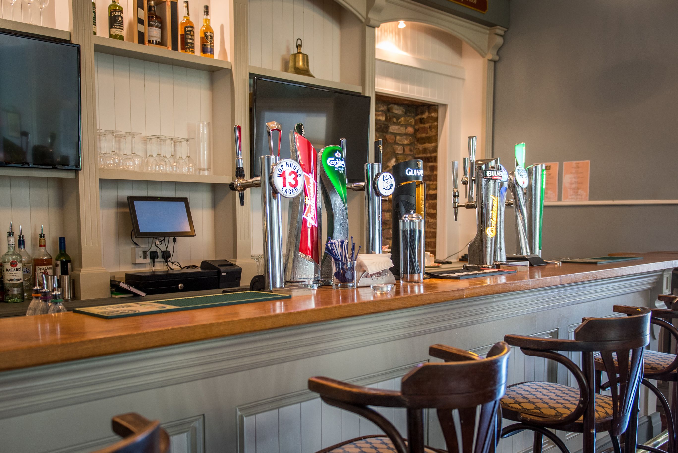 A bar area with multiple beer taps, a cash register, and bar stools.