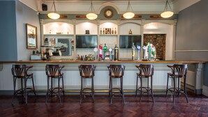 A bar area with a wooden bar counter, four bar stools, and a variety of bottles and glasses.