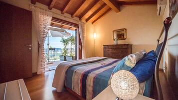 Un dormitorio con techo de madera, una cama con manta a rayas, una lámpara de noche, un aparador y vistas al exterior.