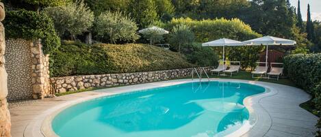 A swimming pool with a stone wall and a wooden deck, surrounded by lush greenery and trees.