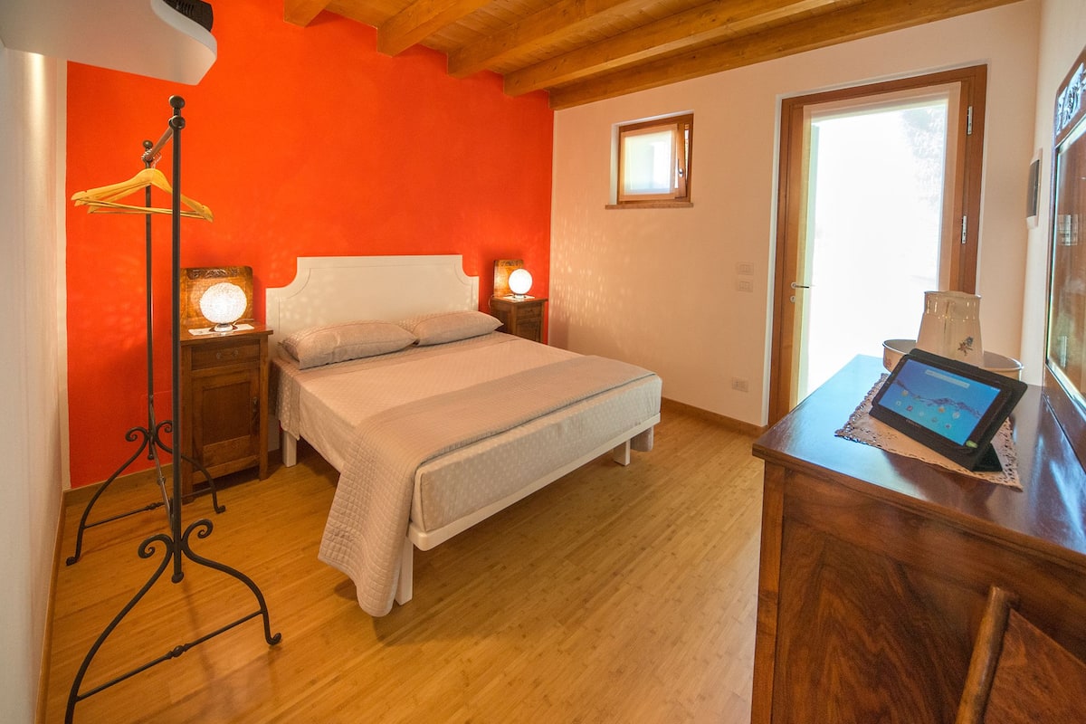 Quarto com cama, mesas de cabeceira, um criado-mudo, cômoda de madeira, abajur e um tablet sobre a cômoda.