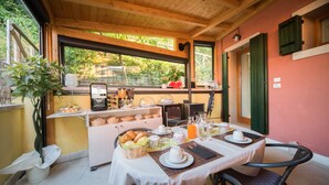 Mesa de desayuno con diversos alimentos, una cafetera y vistas al exterior con vegetación.