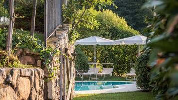 Un muro de piedra con una piscina y sillones de descanso en un jardín exuberante.