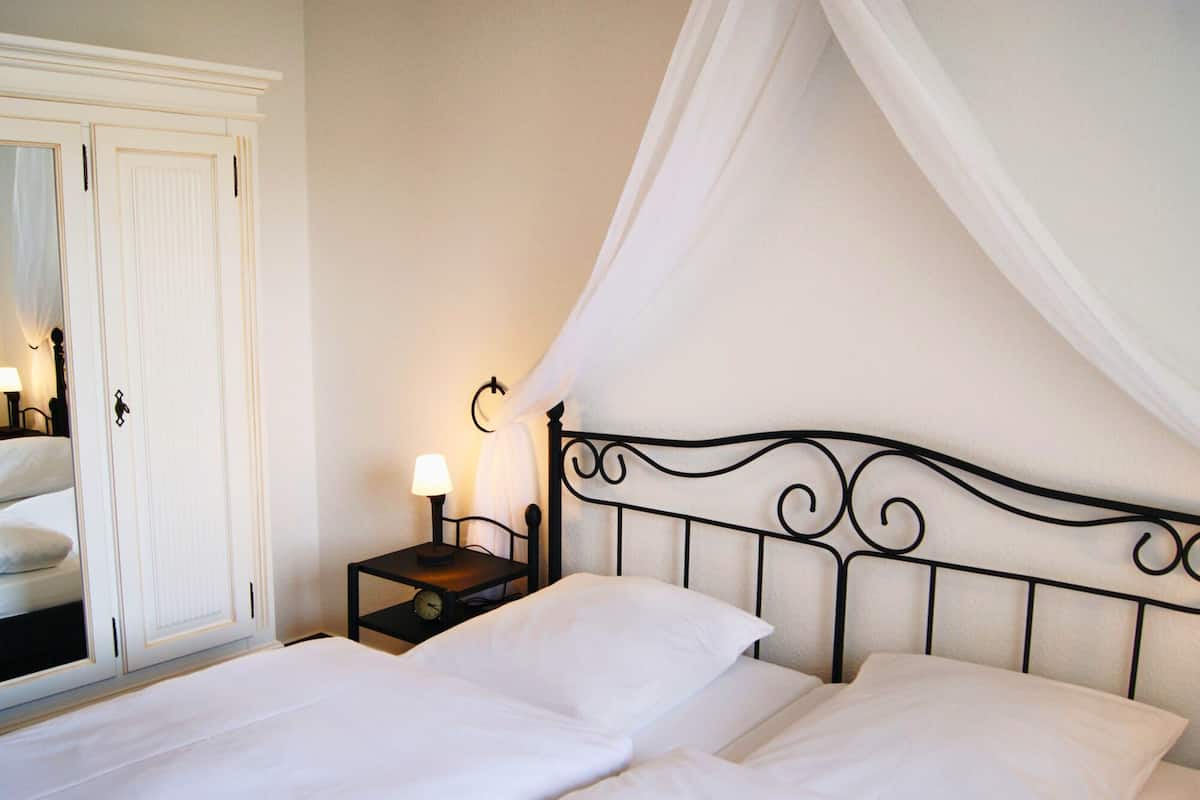 A neatly made bed with white linens, a bedside table with a lamp, and a wardrobe with a mirror.