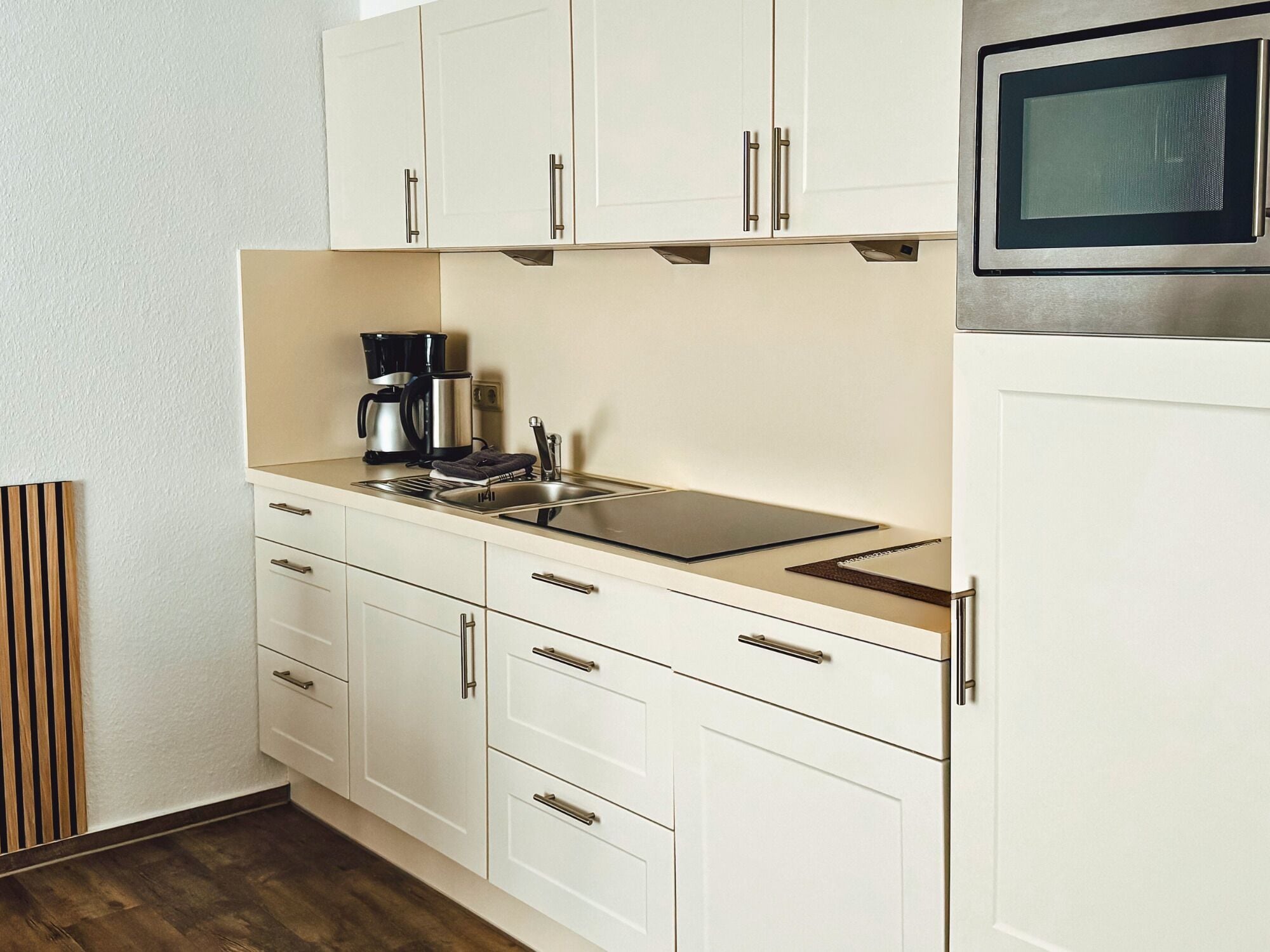 A modern kitchen with white cabinetry, a stainless steel sink, a coffee maker, and a microwave.