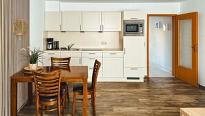 A modern kitchen with white cabinets, a microwave, and a dining area with wooden furniture. - Appartementhaus Gutenberg - Für Paare, Freundinnen & Freunde, Alleinreisende - Parkplatz & WLAN - 2 Min zum See, 6 Min zum Strand (Binz)