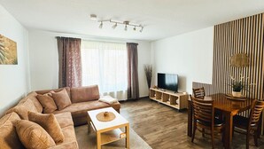 A living room with a sofa, coffee table, TV stand, and dining area with chairs and a table. - Appartementhaus Gutenberg - Für Paare, Freundinnen & Freunde, Alleinreisende - Parkplatz & WLAN - 2 Min zum See, 6 Min zum Strand (Binz)