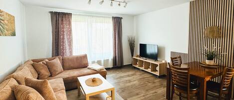 Una sala de estar con sofá, mesa de centro, mueble para televisión y comedor con sillas y una mesa.