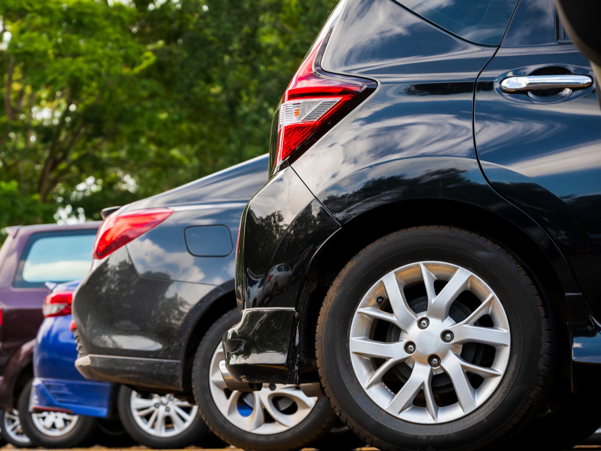 A row of parked cars with visible rear lights and wheel rims.