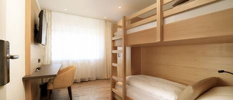 Habitación con literas, escritorio, silla, televisor montado en la pared y ventana con cortinas.