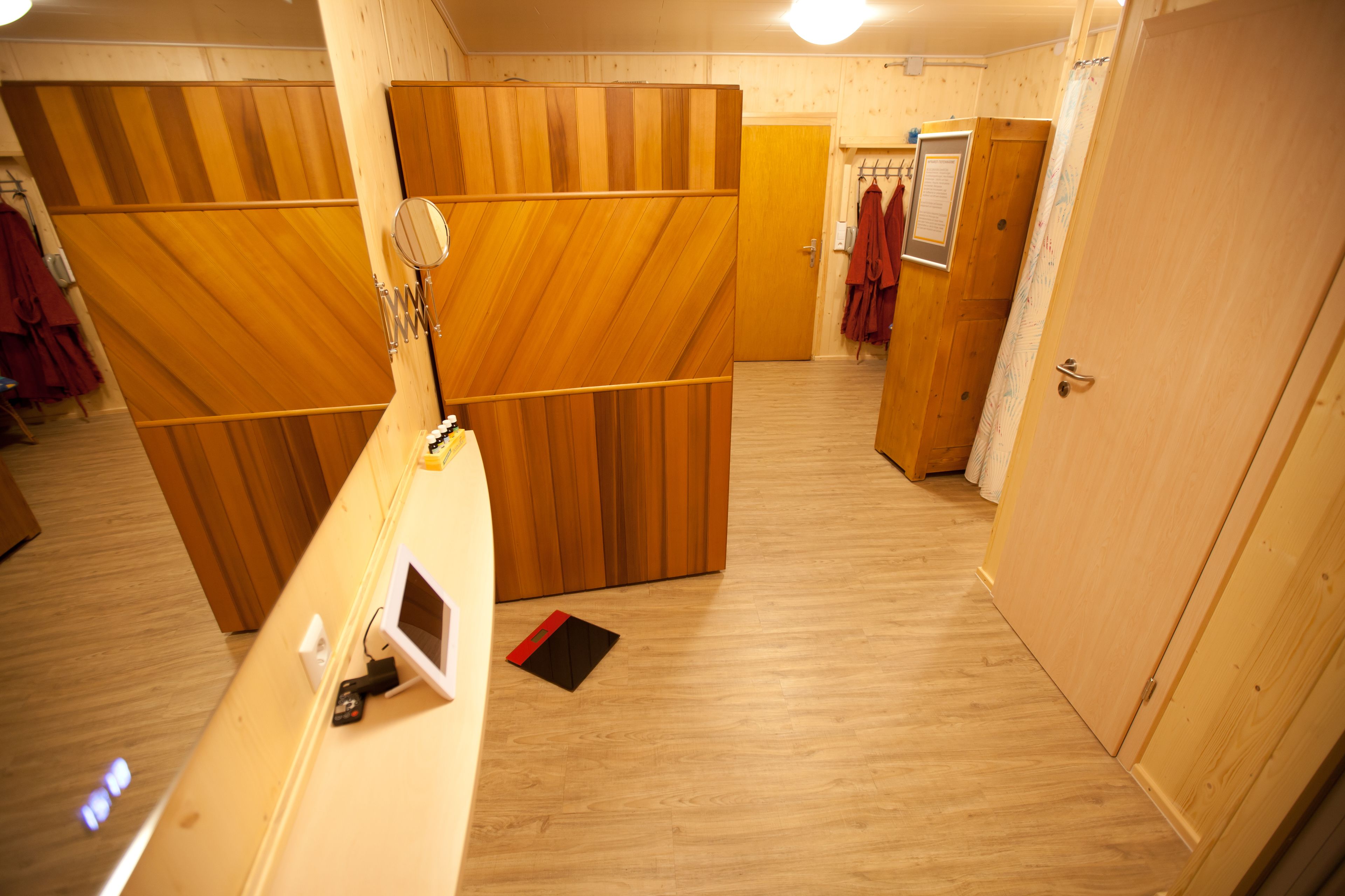 A hotel room with wooden panel walls, a wooden floor, a door, and a coat rack with clothes.