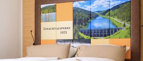 Ein Hotelzimmer mit einem großen Bett, einem Kopfteil mit Panoramablick auf einen See und Berge, und dem Text "LINACHT ALSPERRE 1925".