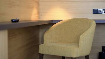 Una habitación moderna con un escritorio de madera, un sillón amarillo, una lámpara colgante negra y un televisor de pantalla plana montado en la pared.