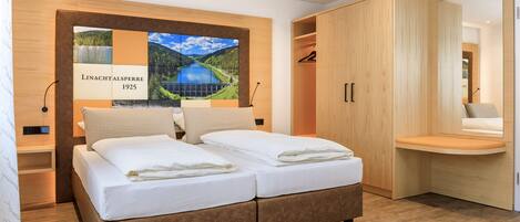 A modern bedroom with a large bed, wooden wardrobe, and a wall-mounted artwork.