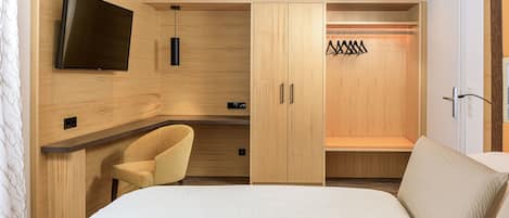 Un dormitorio con cama, una silla, televisor montado en la pared y un armario de madera.