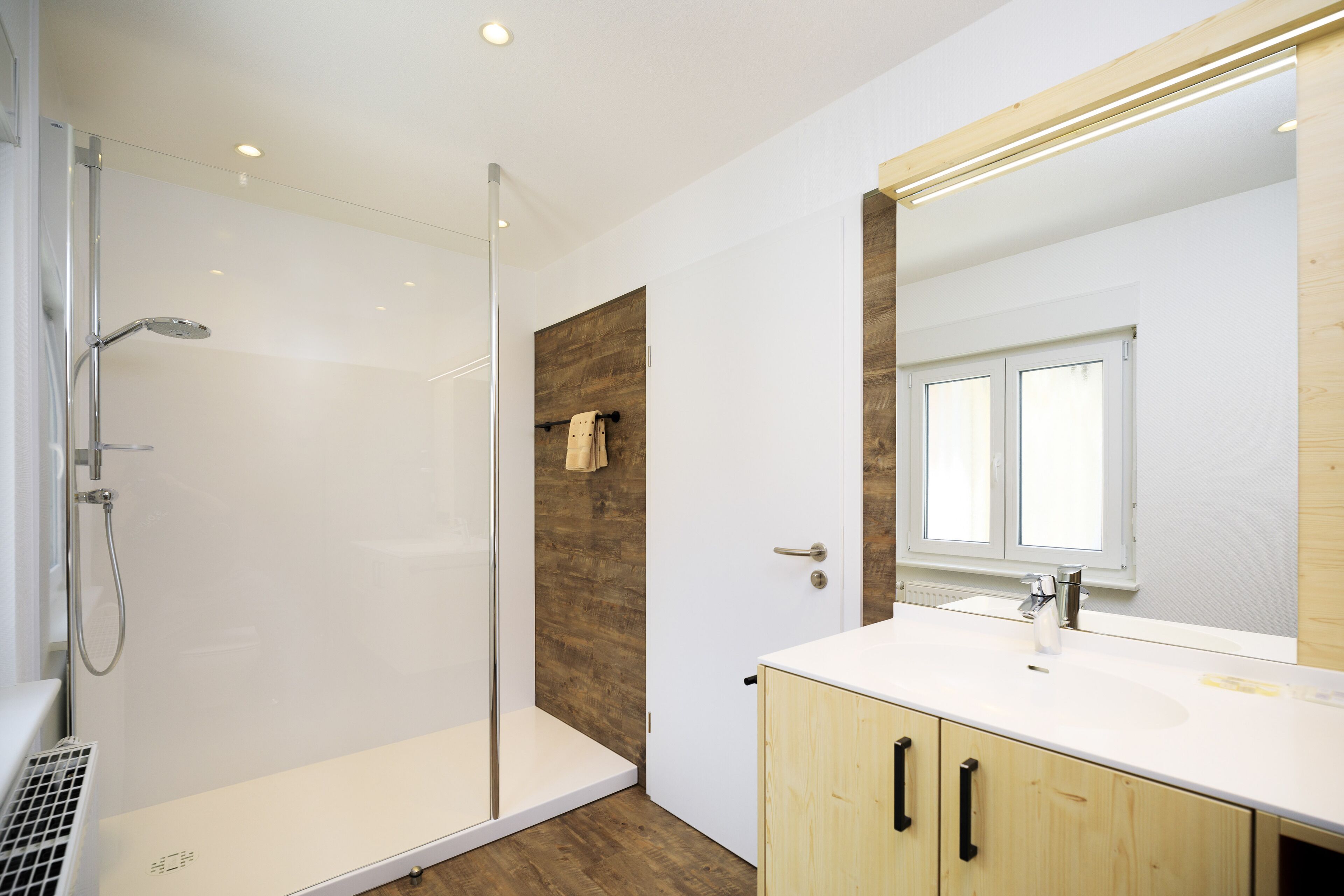 A modern bathroom with a glass shower enclosure, a wooden accent wall, and a large mirror above the sink.