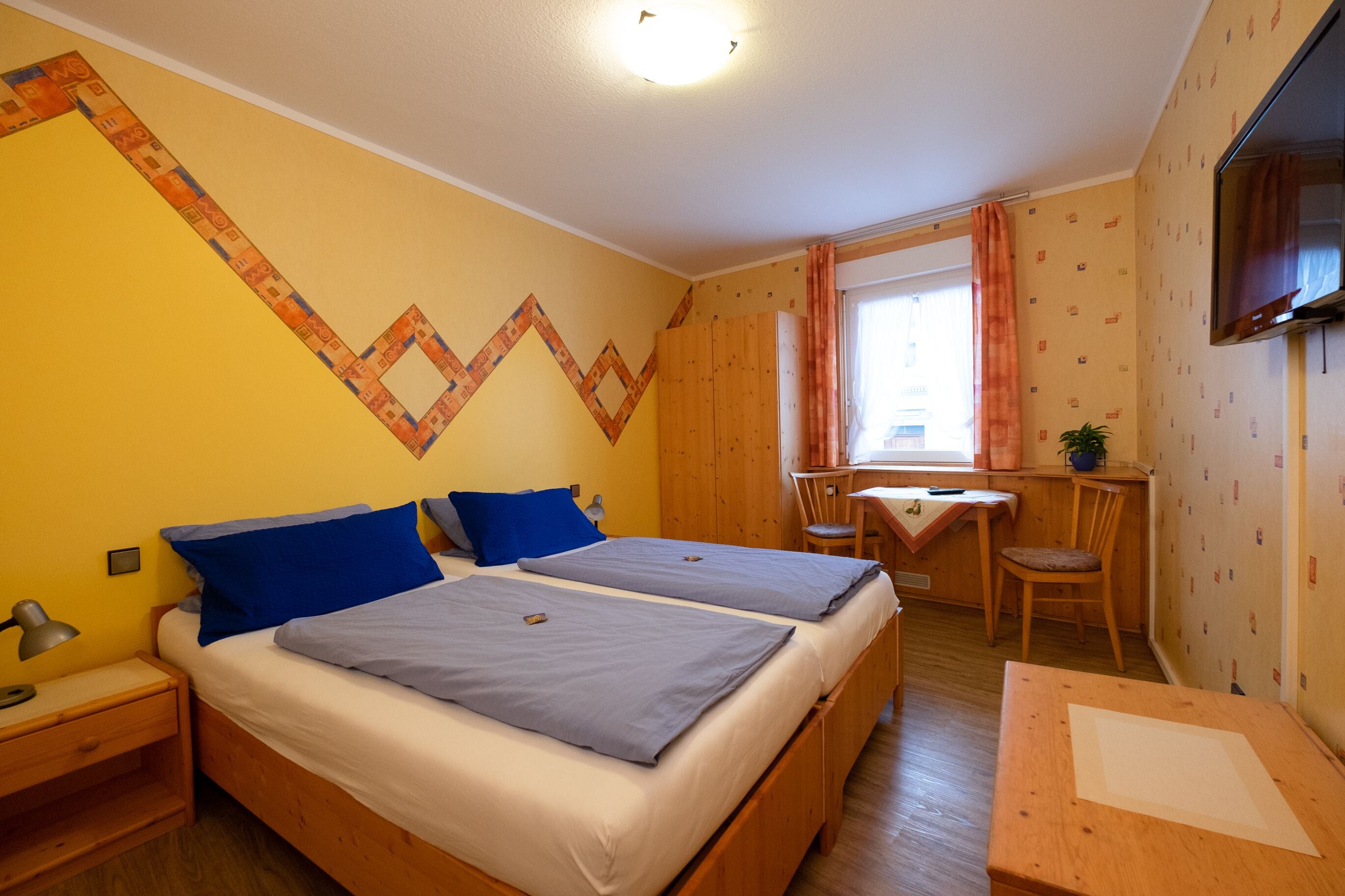 Een kamer met twee bedden, een bureau, een stoel, een televisie en een raam met gordijnen.