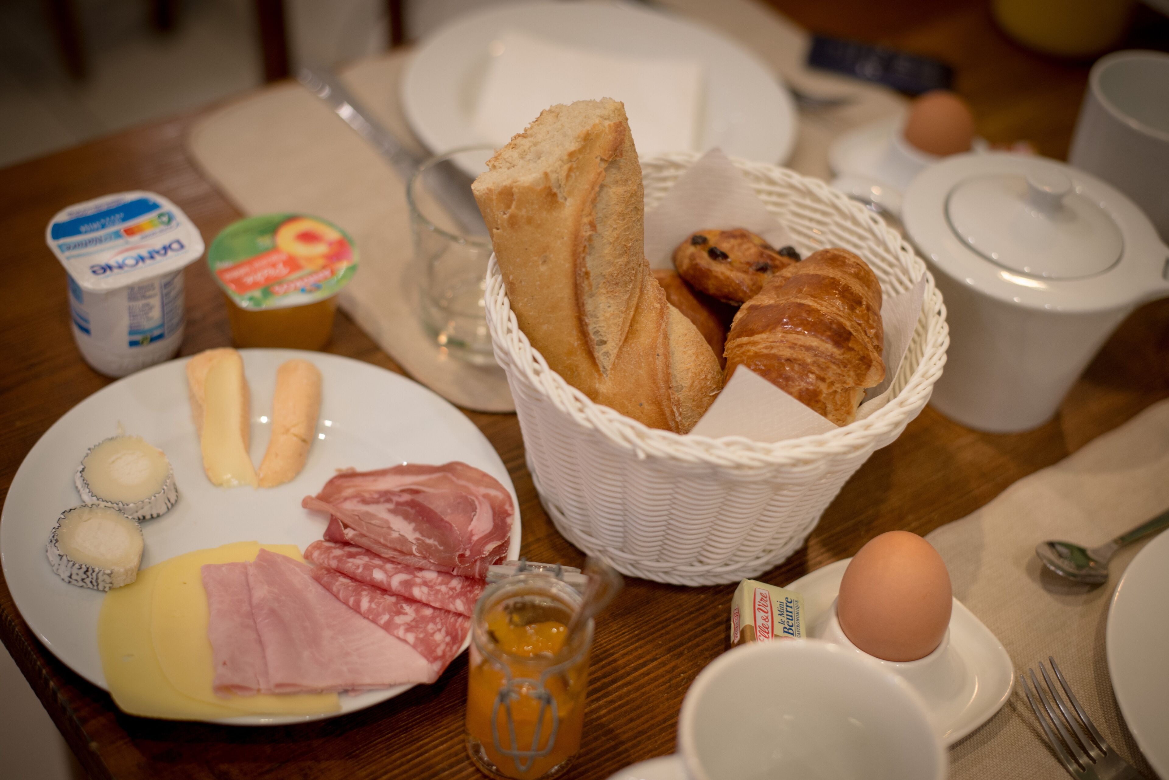 A breakfast table with plates of food, a basket of bread, and a jug of juice.