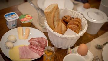 A breakfast table with plates of food, a basket of bread, and a jug of juice.