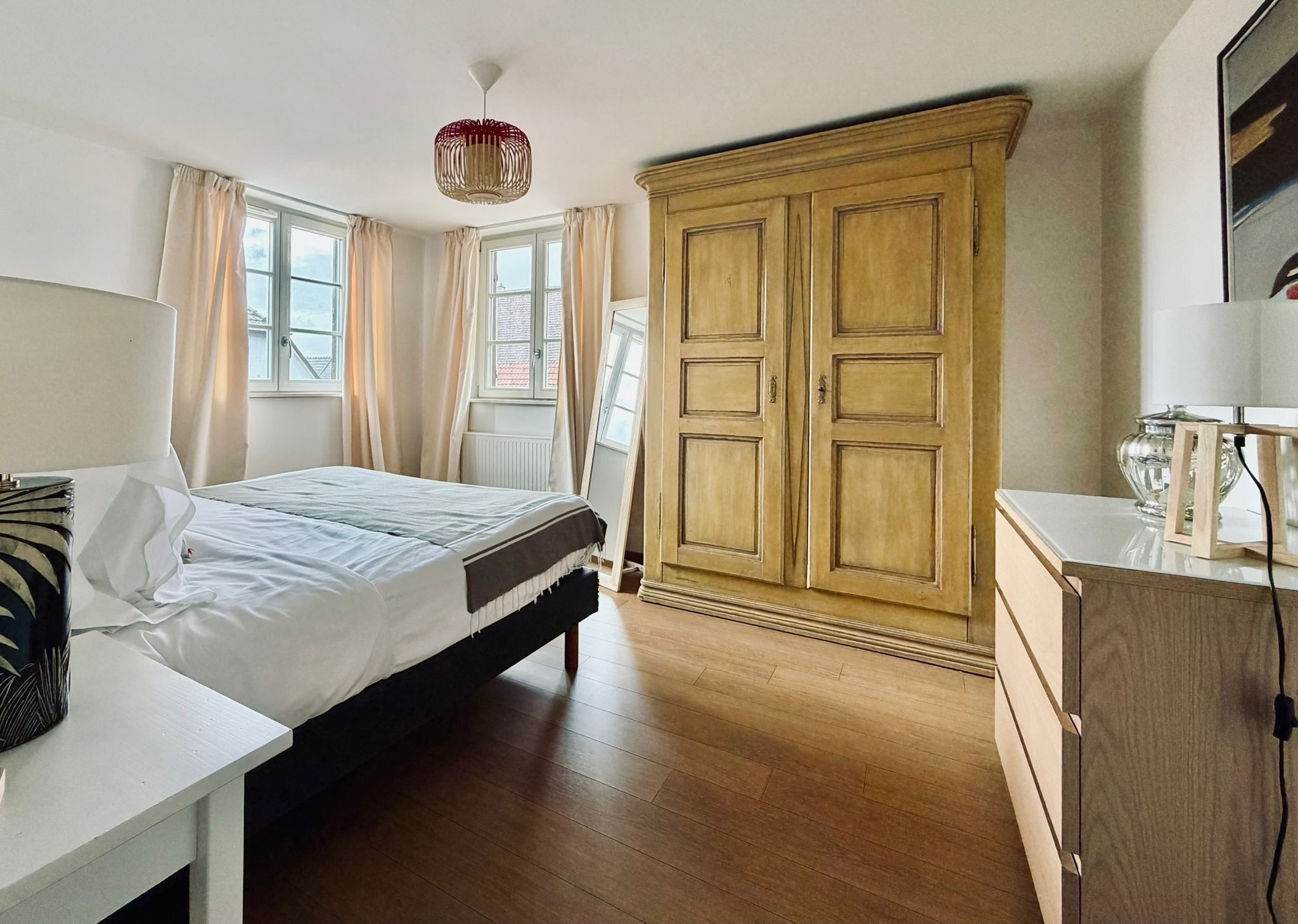 A bedroom with a bed, a dresser, a wardrobe, and a window with curtains.