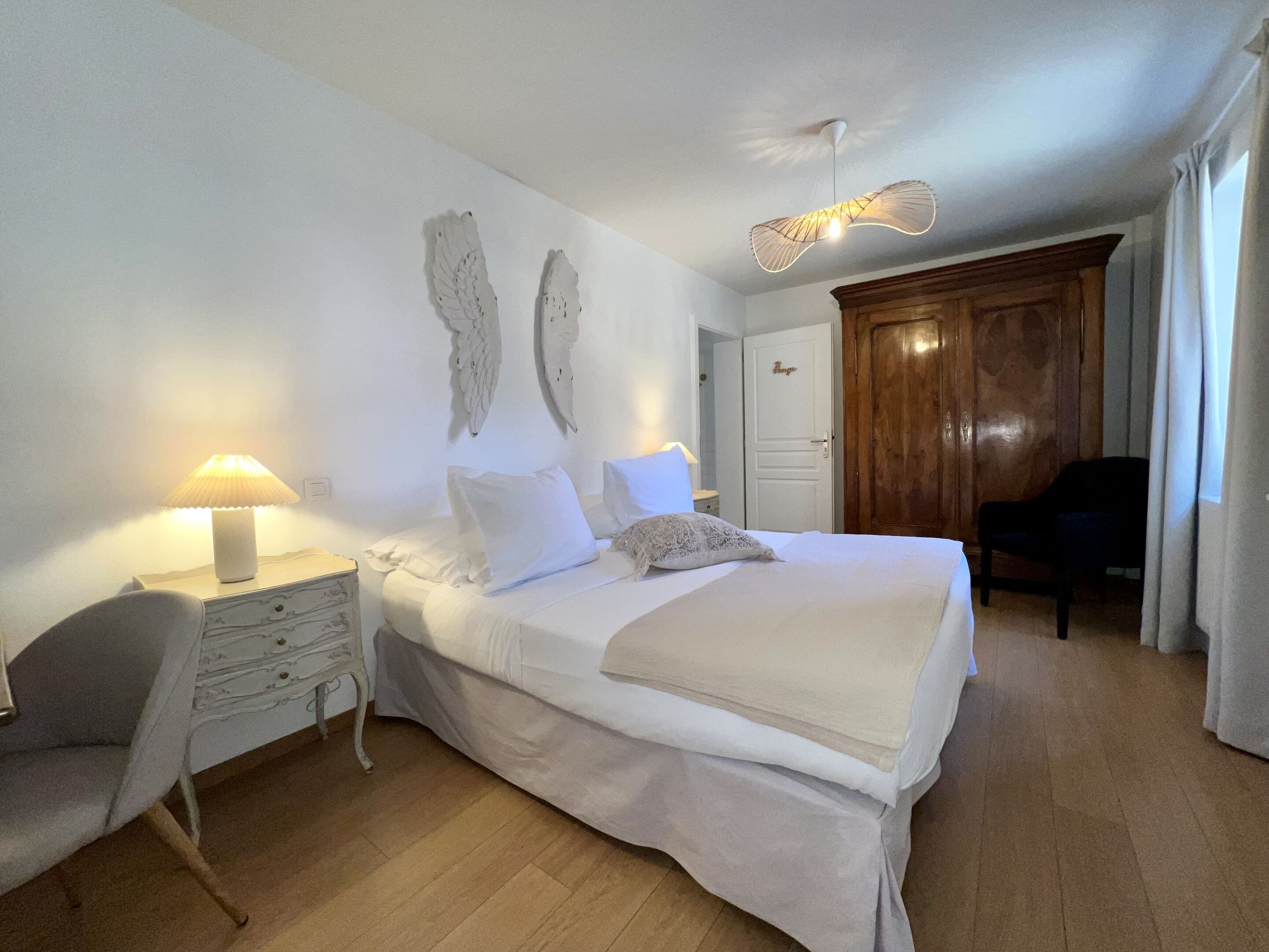 A bedroom with a bed, a nightstand with a lamp, a chair, and a wooden wardrobe.