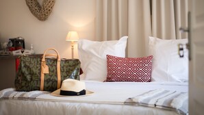 A neatly made bed with white linens, a patterned pillow, a hat, and a Louis Vuitton bag. - Hameau D'eguisheim (Eguisheim)