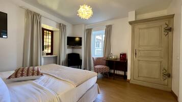 Una habitación de hotel con cama, televisión, escritorio y silla, armario y candelabro.
