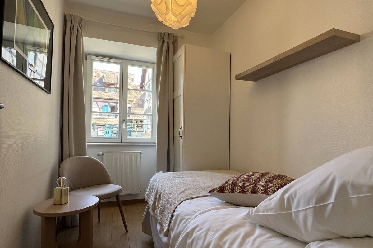 Een slaapkamer met een bed, een stoel, een tafel, een hanglamp en een raam.