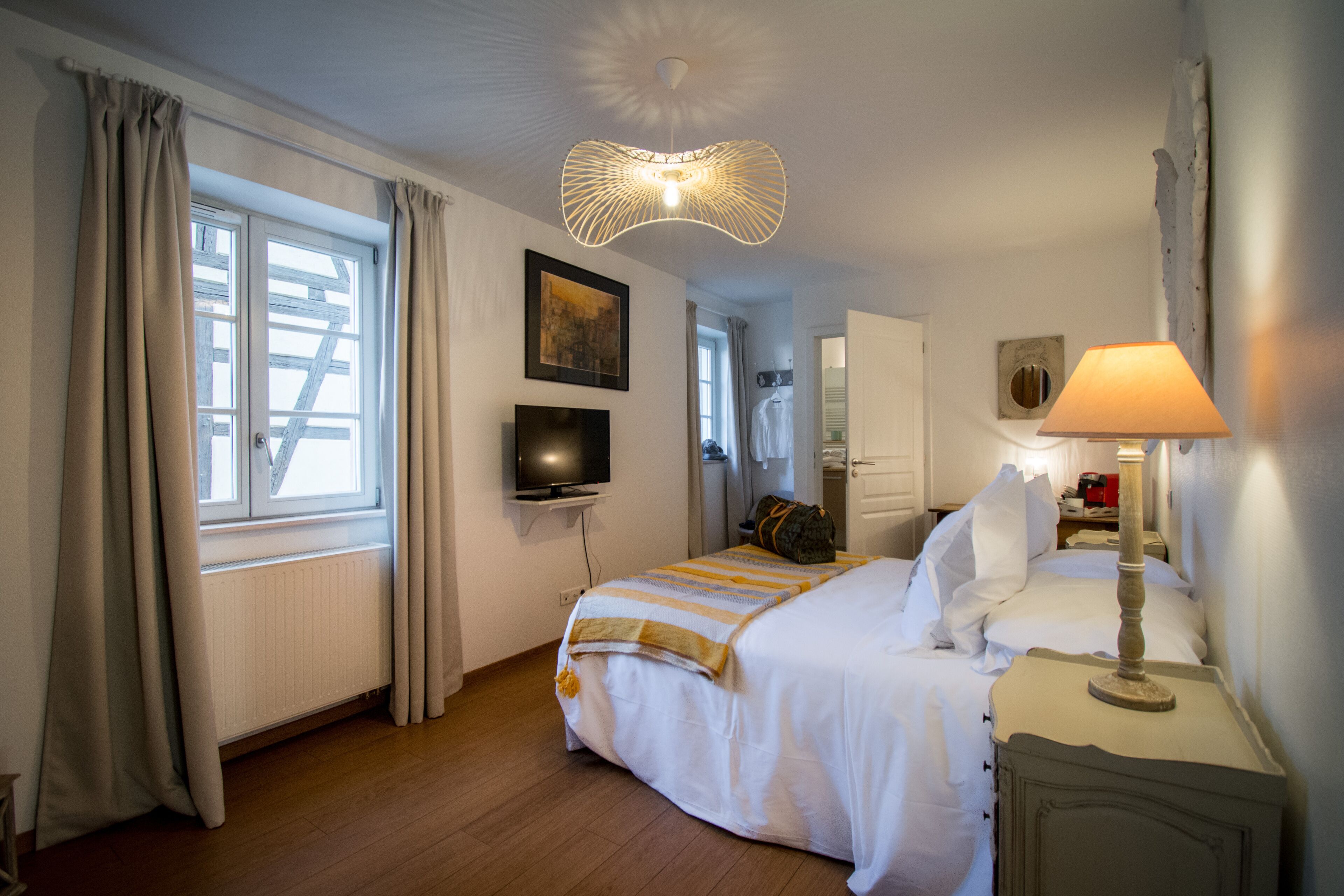Une chambre d’hôtel avec un lit, une télévision, une lampe et une fenêtre avec des rideaux.