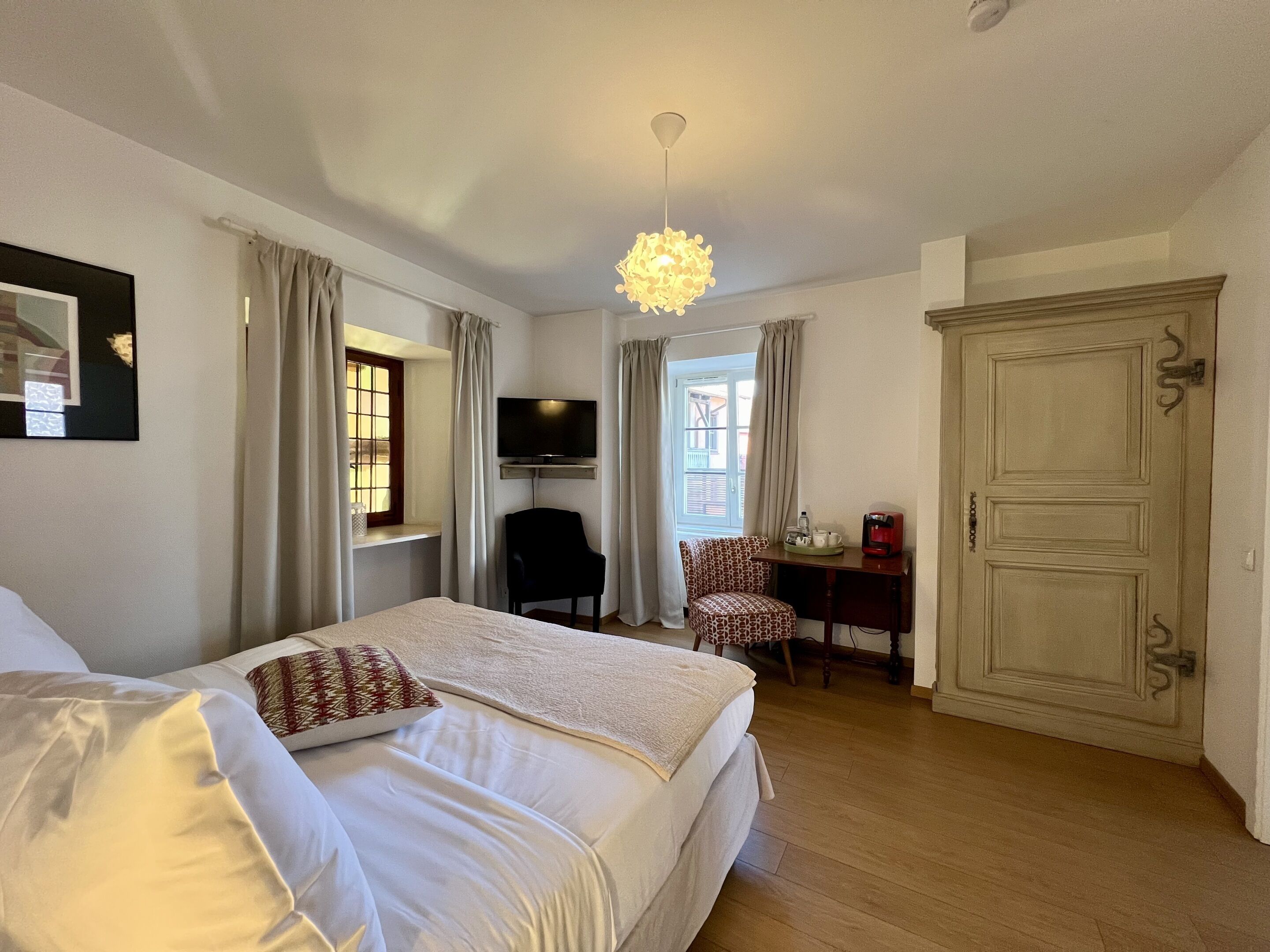 A hotel room with a bed, a desk, a chair, a television, and a wardrobe.