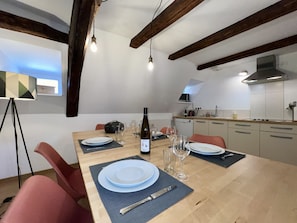 Un comedor con una mesa de madera preparada para cuatro personas, una botella de vino y copas.