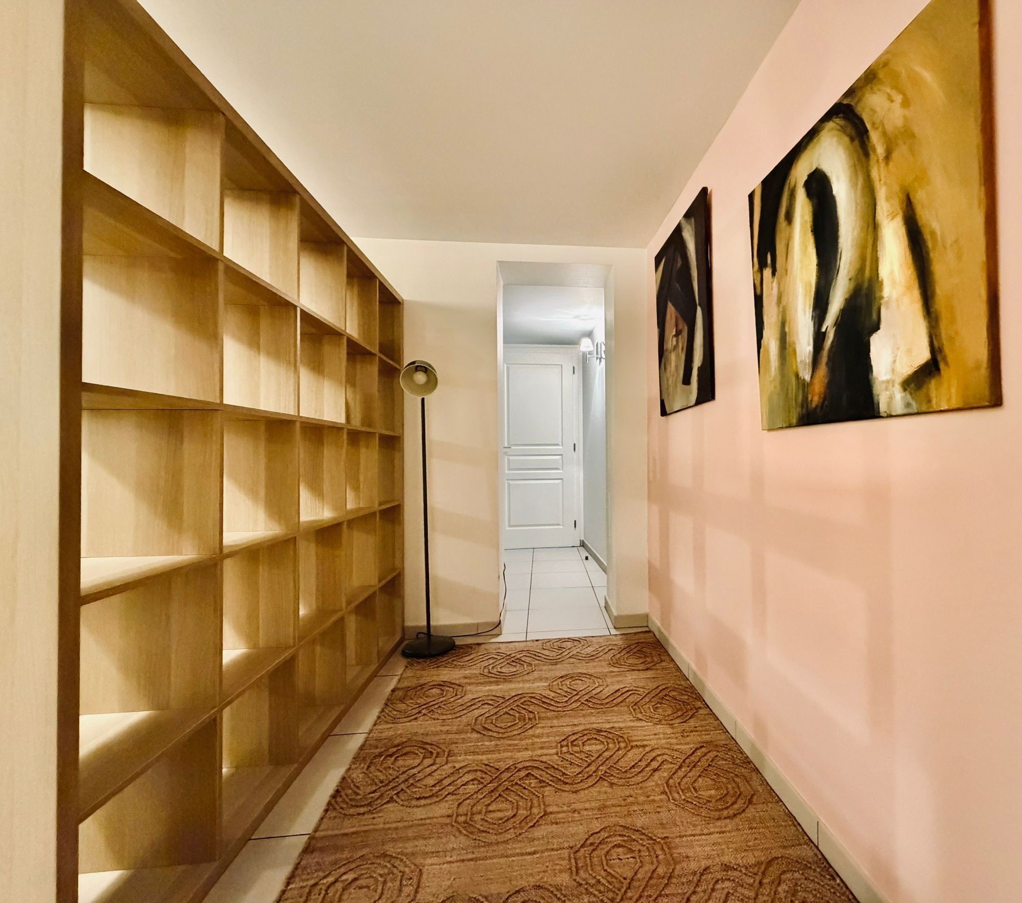 Ein Flur mit Teppichmuster, Holzbögen und zwei abstrakten Gemälden an der Wand.