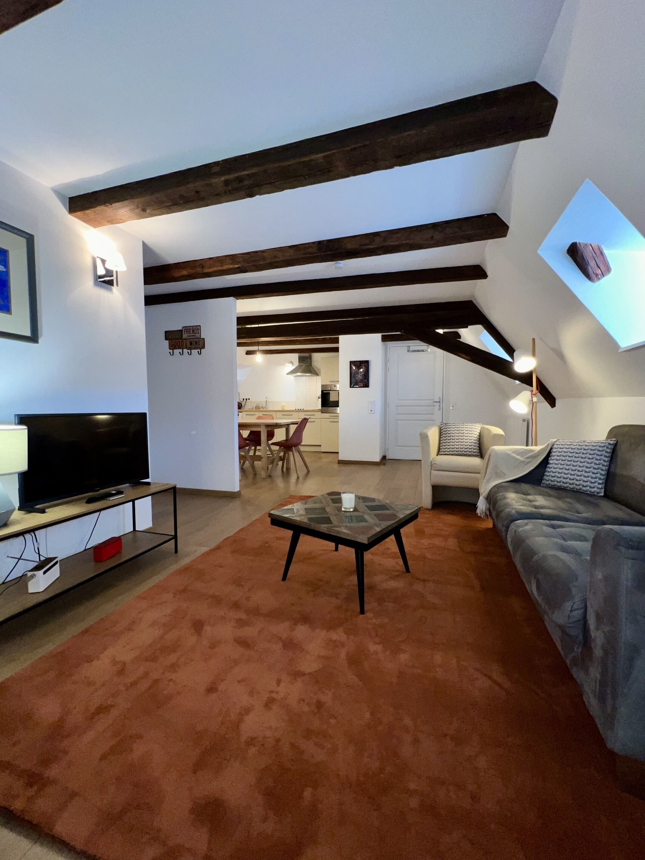 A living room with a TV, sofa, and coffee table. There is a kitchen in the background.