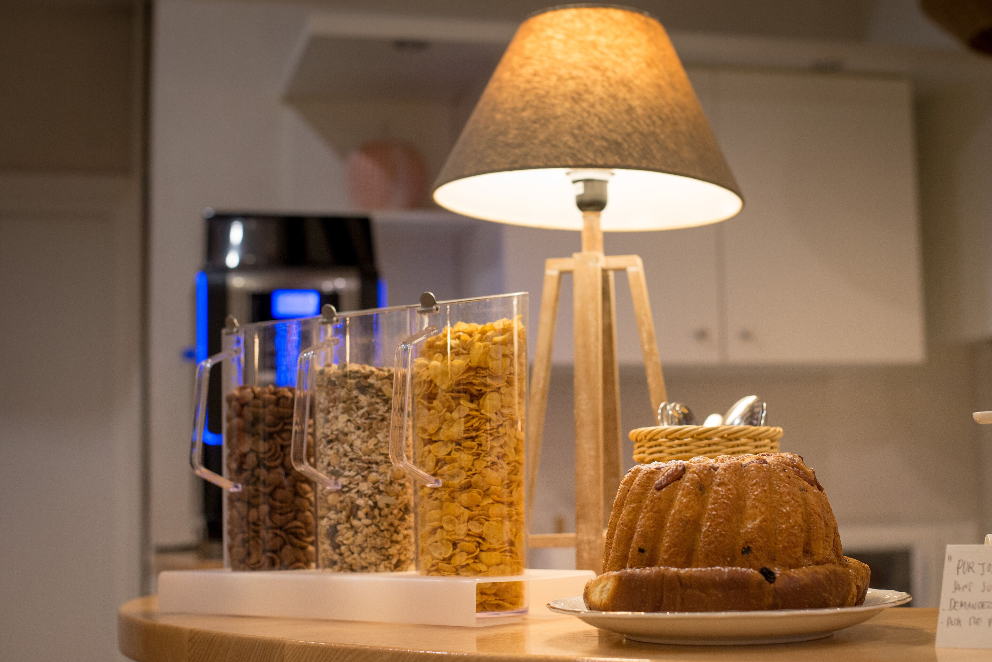 A breakfast display with cereal containers, a lamp, and a bundt cake on a table.