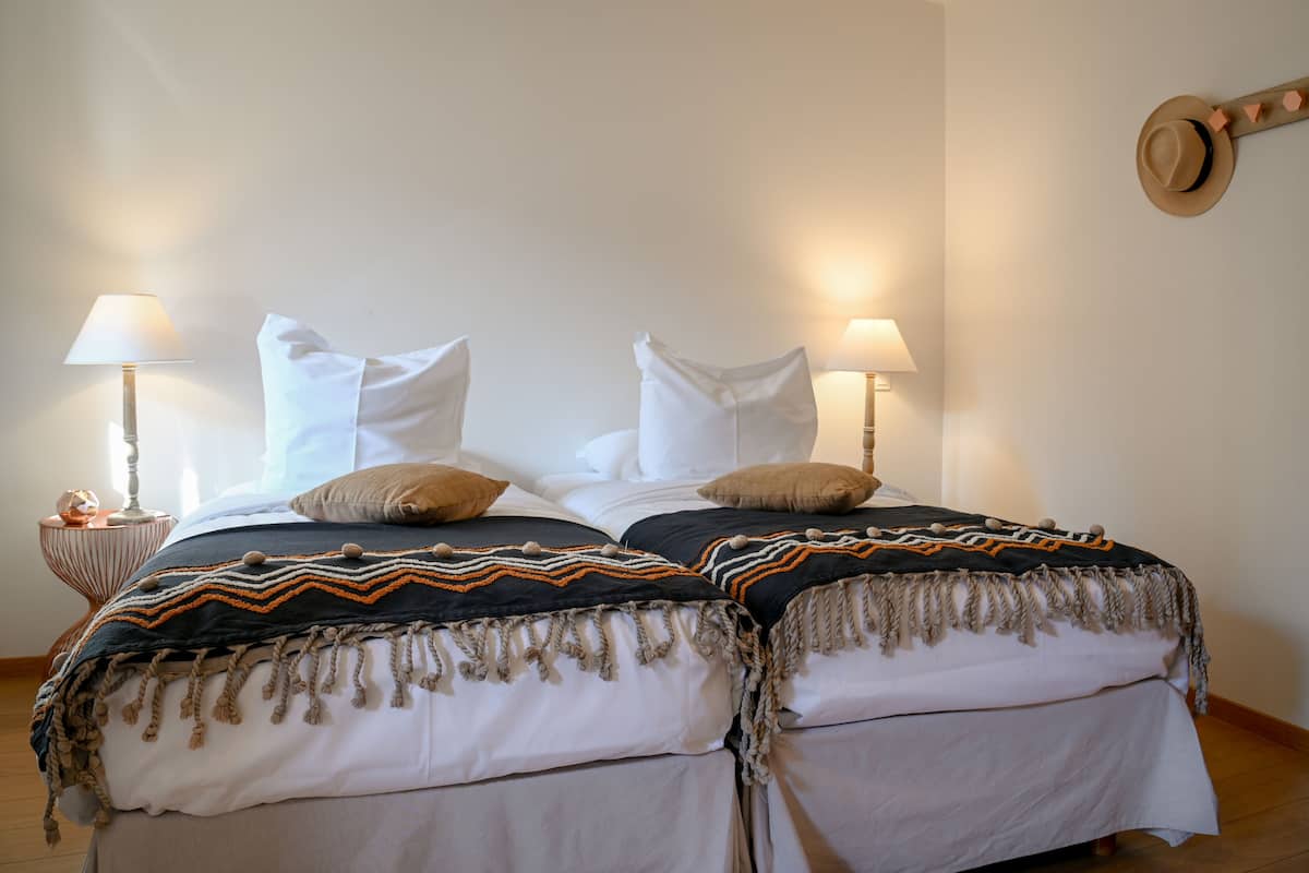 Een tweepersoonsbed met witte lakens en twee lampen aan weerszijden.