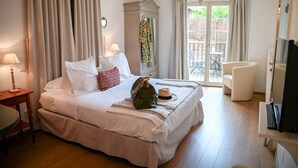 A neatly made bed with white linens, a bedside table with a lamp, a wardrobe, a chair, and a television. - Hameau D'eguisheim (Eguisheim)