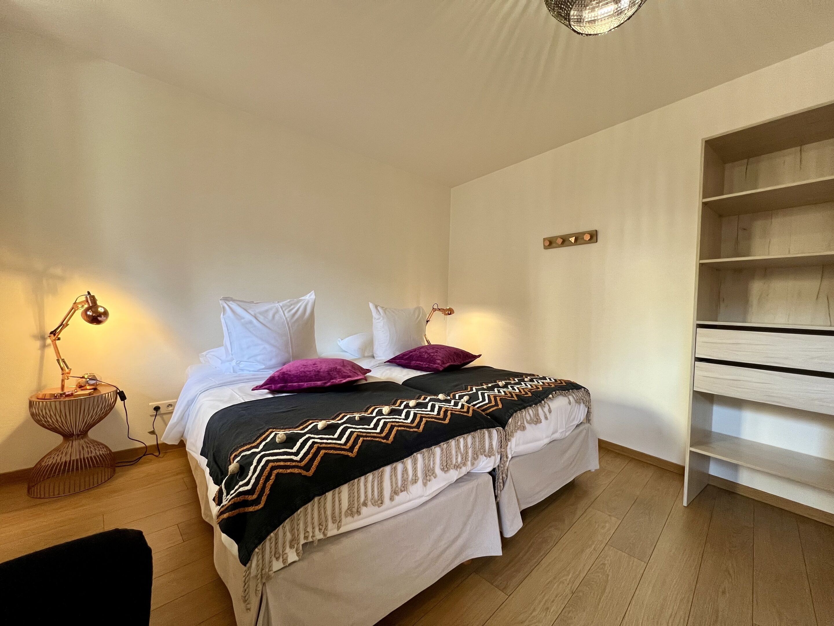 A bedroom with a bed, a bedside lamp, a wooden floor, and a built-in shelf.