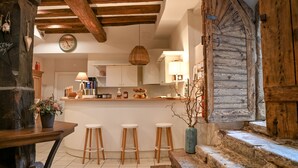 A rustic kitchen with wooden beams, a bar area with stools, and a large wooden door. - Hameau D'eguisheim (Eguisheim)
