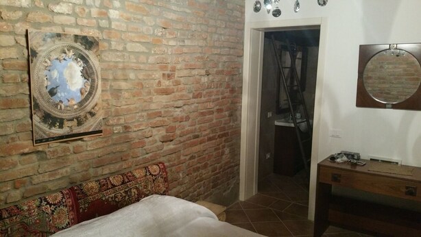 A room with a brick wall, a bed with a patterned headboard, a wooden dresser, and a mirror on the wall. - B&B All'Aeroporto (Curtatone)