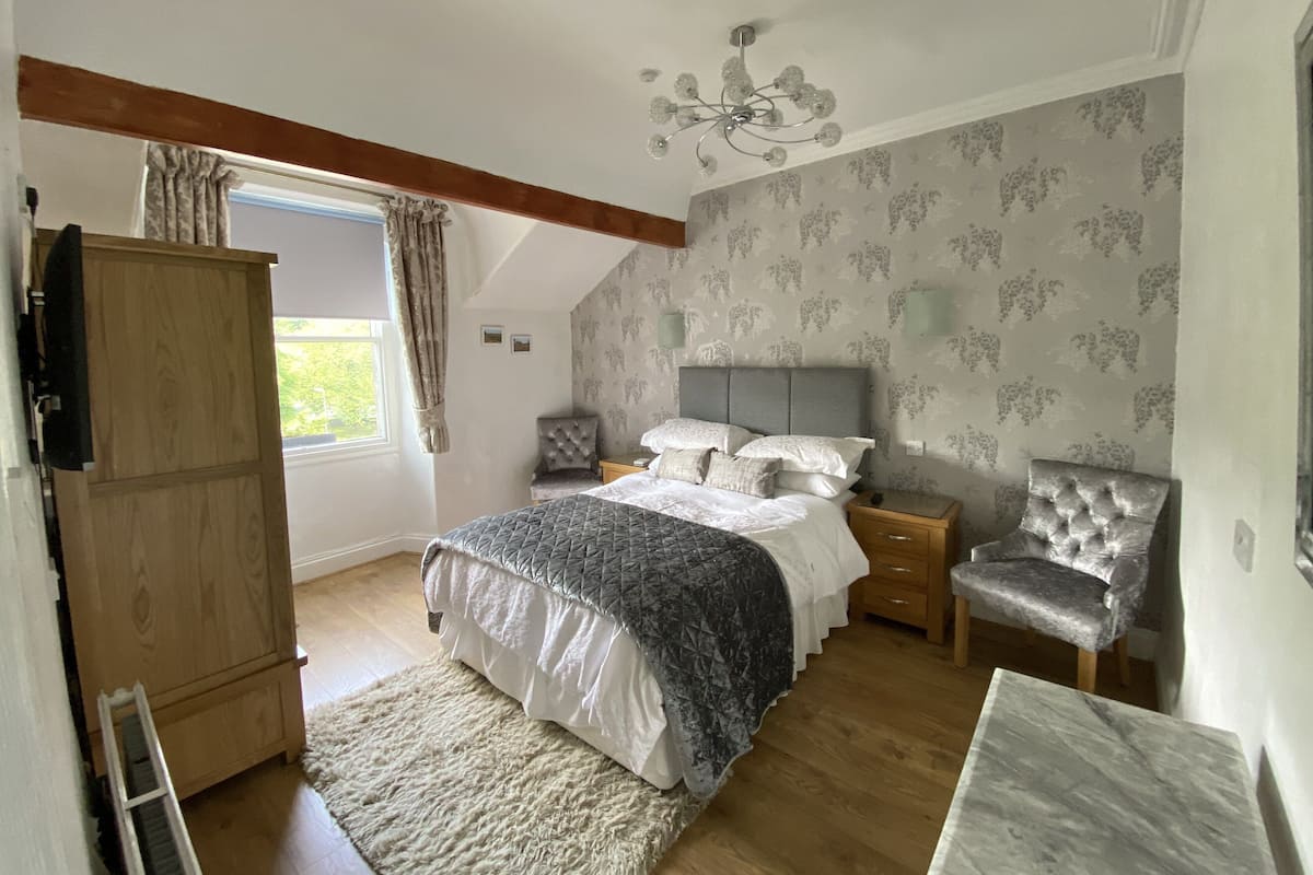 Quarto com cama, guarda-roupa, cadeira, mesa de cabeceira, candelabro e janela com cortinas.
