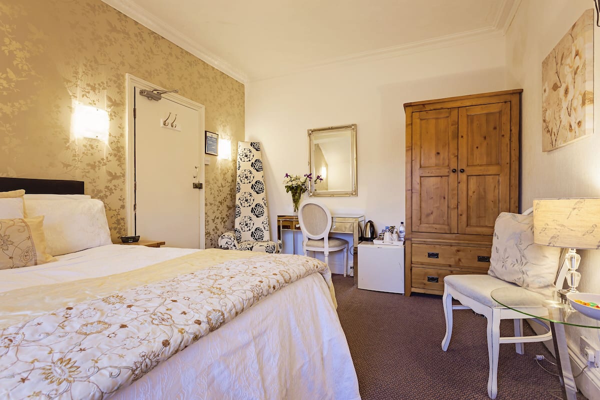 Quarto de hotel com uma cama, uma mesa, uma cadeira, um guarda-roupa e um espelho.