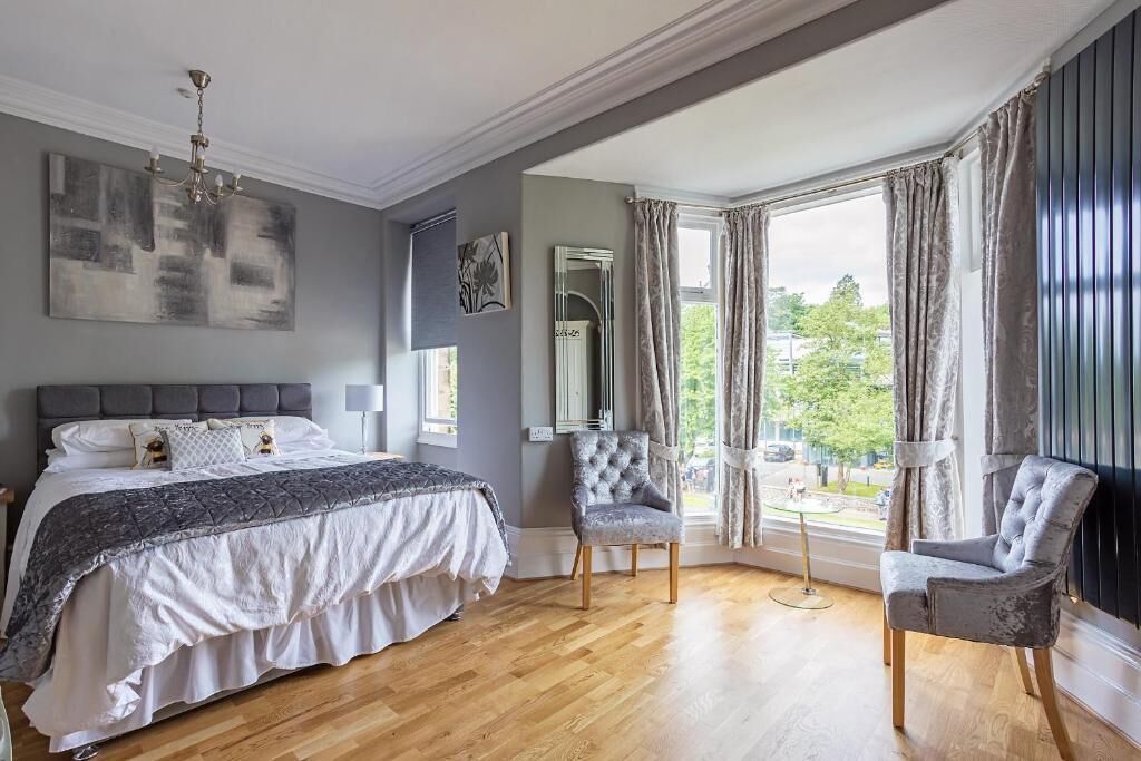A bedroom with a large bed, a chair, a mirror, and a view of the outdoors.