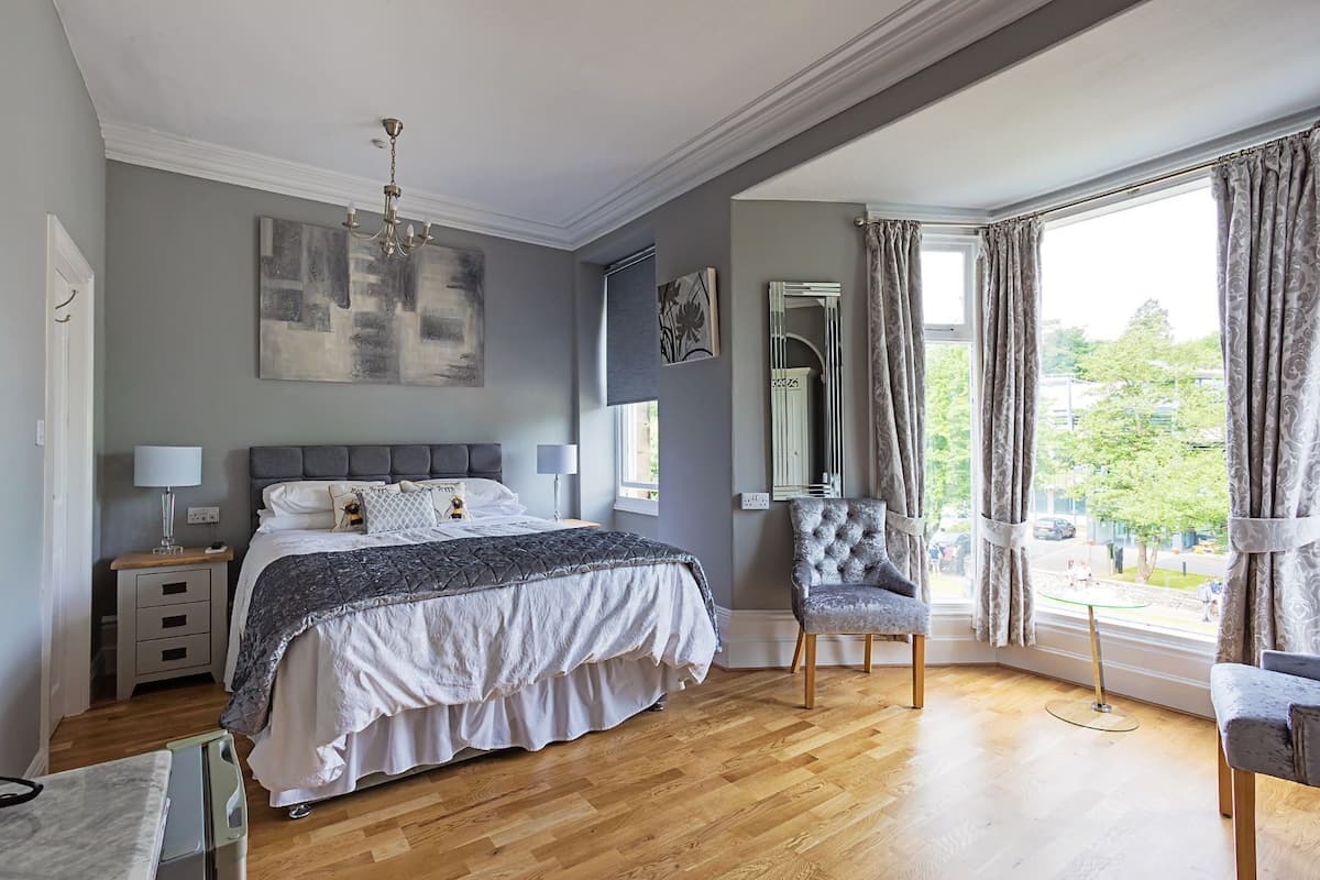Um quarto com uma cama, mesas de cabeceira, uma cadeira, um espelho e uma janela com cortinas.