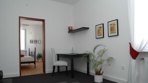 A modern living room with a black dining table, a white armchair, a potted plant, and a bookshelf with books and a small orange box. - Hotel Scheffelhof (Waldkirch)