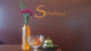 A vase with flowers, a glass bowl, and a bell on a table against a wall with the text "Scheffelhof". - Hotel Scheffelhof (Waldkirch)